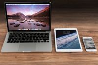 A Macbook, iPad, and iPhone side by side on a table. 